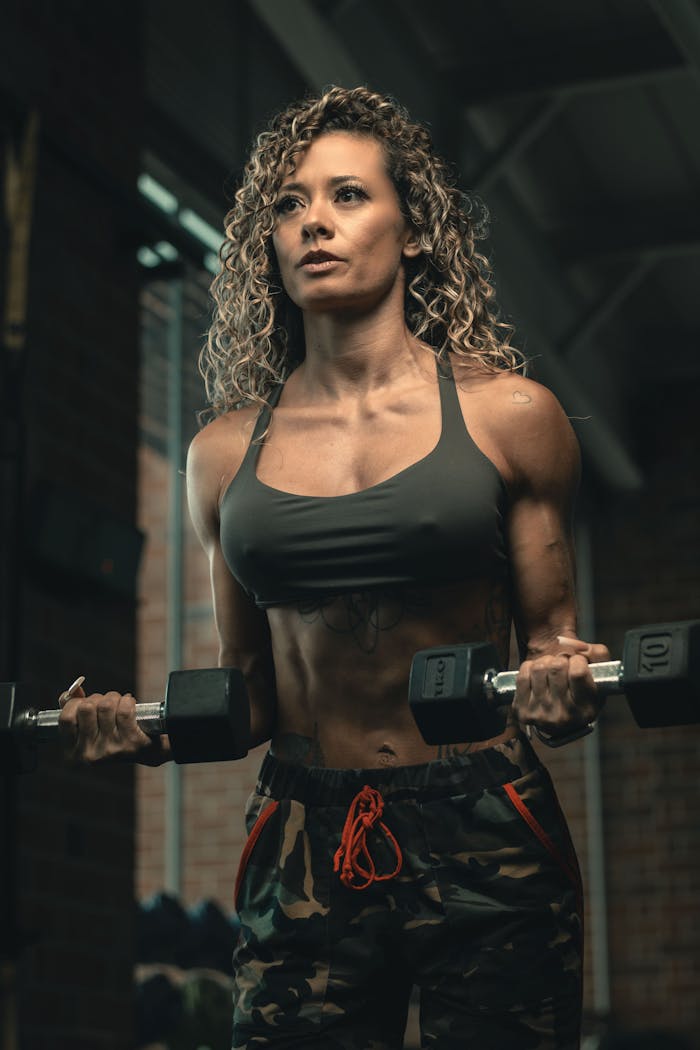 Athletic woman exercises with dumbbells in a gym setting, showcasing strength and dedication.