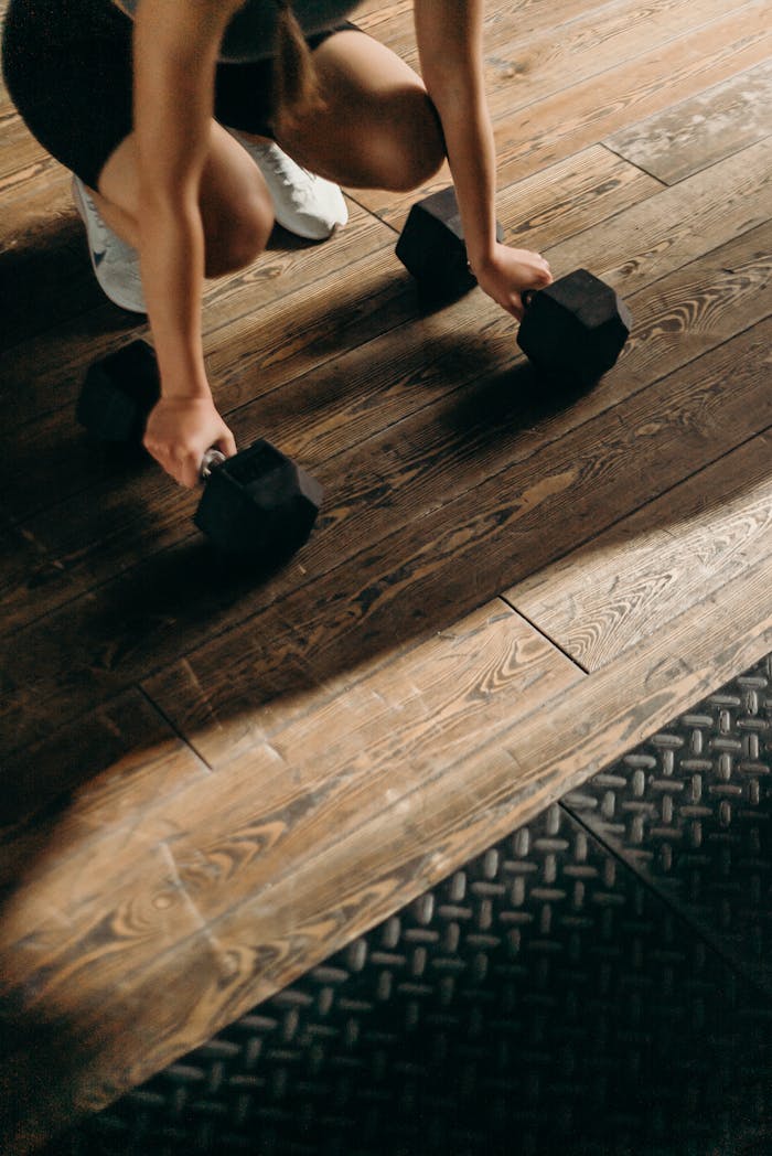 Home Female gym-goer in action with dumbbells on wooden floor, ready to lift.
